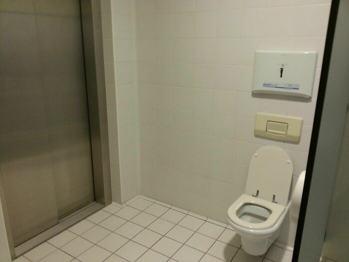 Questionably designed bathroom with toilet positioned next to elevator door