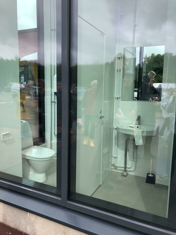 Bathroom with toilet and sink fully visible through large glass window