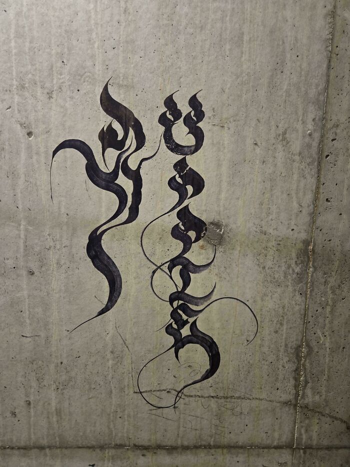 Abstract black calligraphy on a concrete wall. This interesting post leaves one wondering, What does this mean?