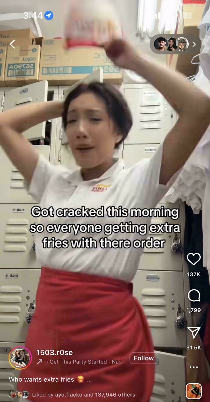 A worker in a white shirt and red apron raises her arms in a locker room, posting something interesting about fries.