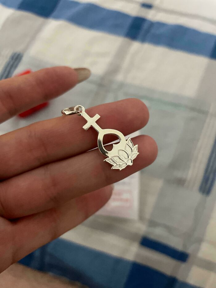 A hand holds a silver pendant shaped like the Venus symbol merging with a lotus flower, something interesting.