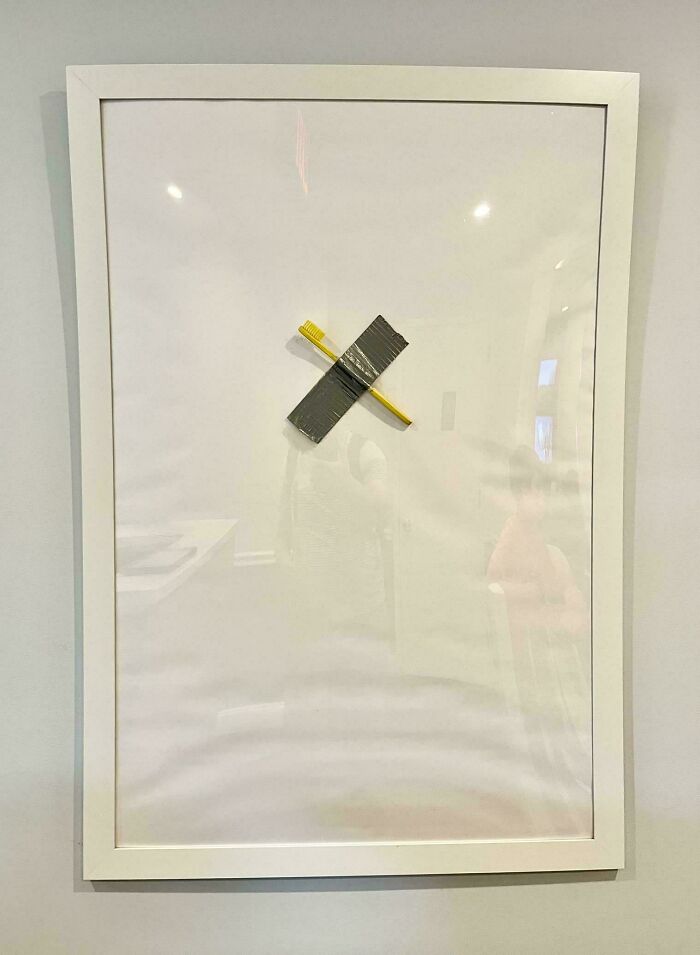 A yellow toothbrush taped to a white board in a white frame, demonstrating doctors awesome sense of humor.