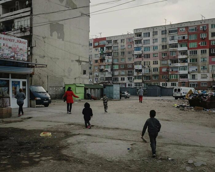 Urban hell with rundown apartment buildings and people in bleak, empty courtyard