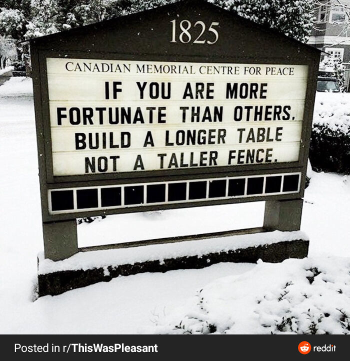 A wholesome pic of a Canadian Memorial Centre sign in snow, displaying the message: Build a longer table, not a taller fence.