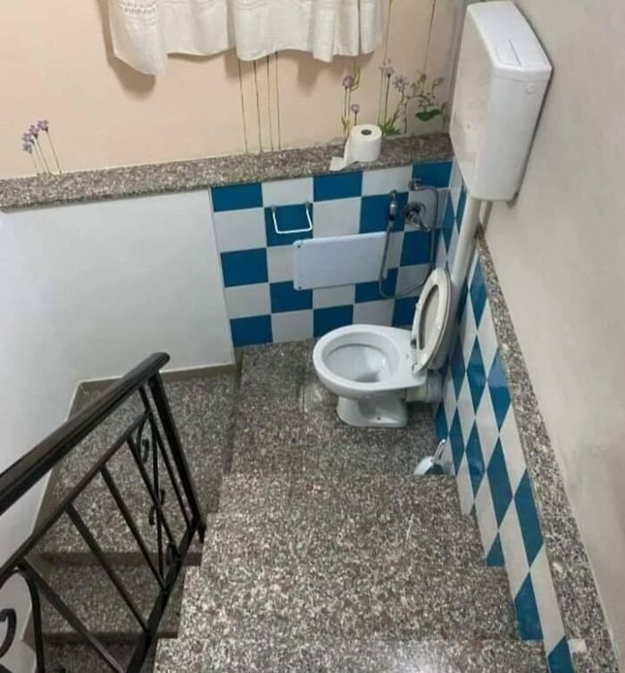 Bathroom toilet placed at the bottom of a staircase in a questionably designed bathroom