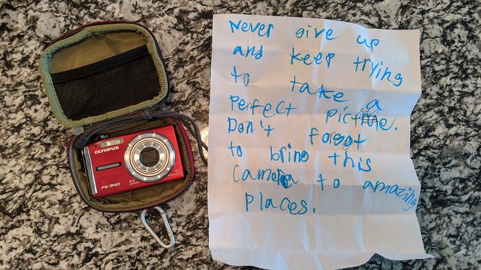 A red Olympus camera in a case next to a handwritten note, conveying wholesome pics and encouragement.
