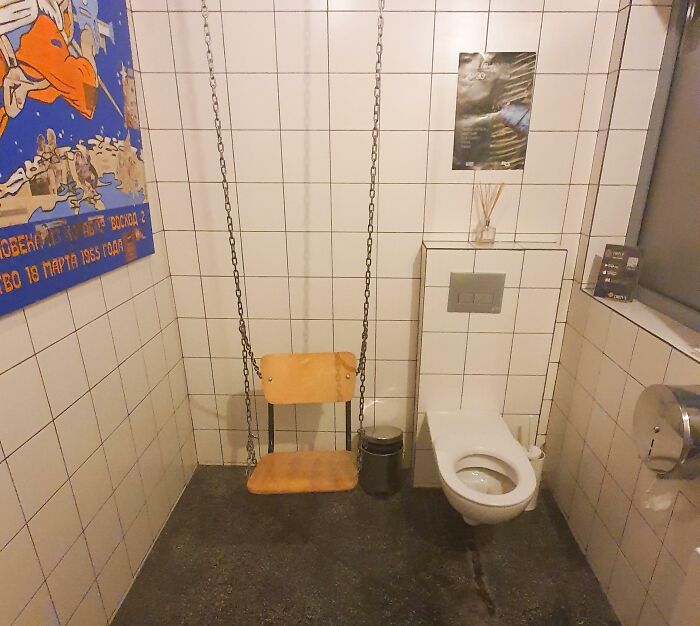 Bathroom with wooden swing next to tiled toilet and wall posters