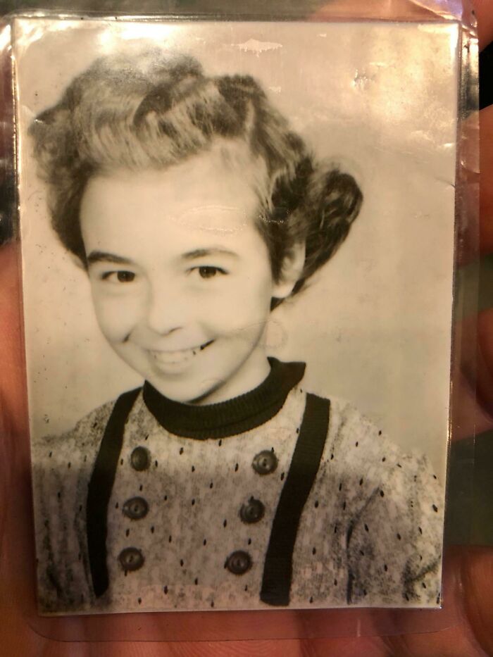 A black and white photo of a smiling young girl with curly hair and a patterned sweater. A wholesome pic from childhood.
