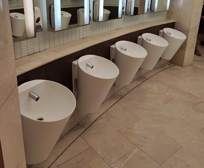 Curved urinals with awkward angles in questionably designed bathroom