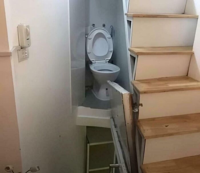 Toilet positioned awkwardly in a narrow space under a staircase with limited access