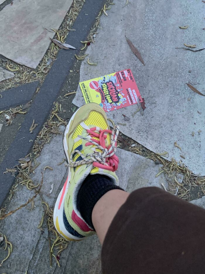 A sneaker with yellow, pink, and blue accents next to a vibrant red and yellow flyer on a gray tiled ground, an accidental color match.