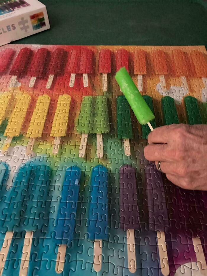 A hand holds a green popsicle over a rainbow popsicle puzzle, featuring wholesome pics of sweet treats.
