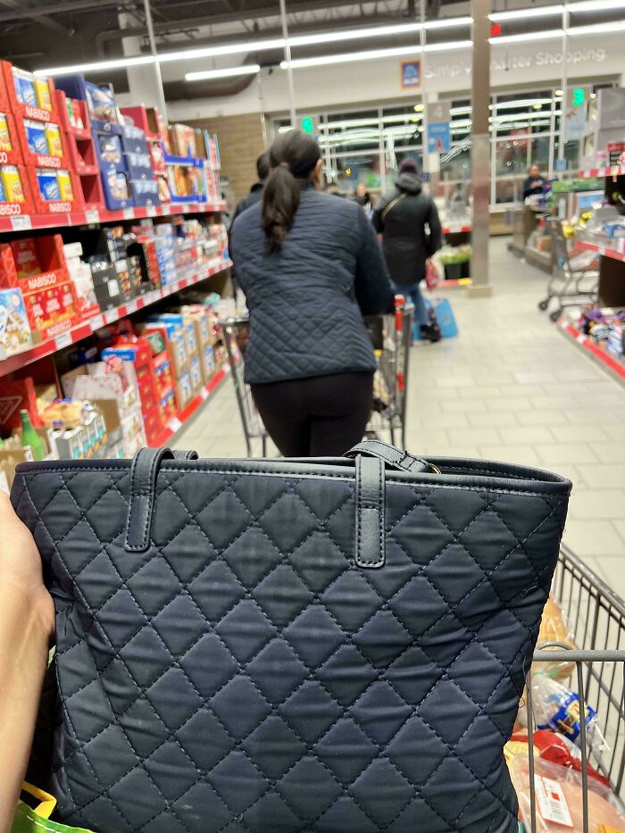 A shopper's dark quilted bag accidentally color matches a person's quilted jacket ahead in a grocery aisle. Satisfying color matches.