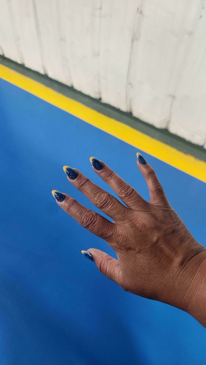 A hand with dark blue and yellow-tipped nails perfectly matches the blue wall and yellow strip above it, accidental color match.