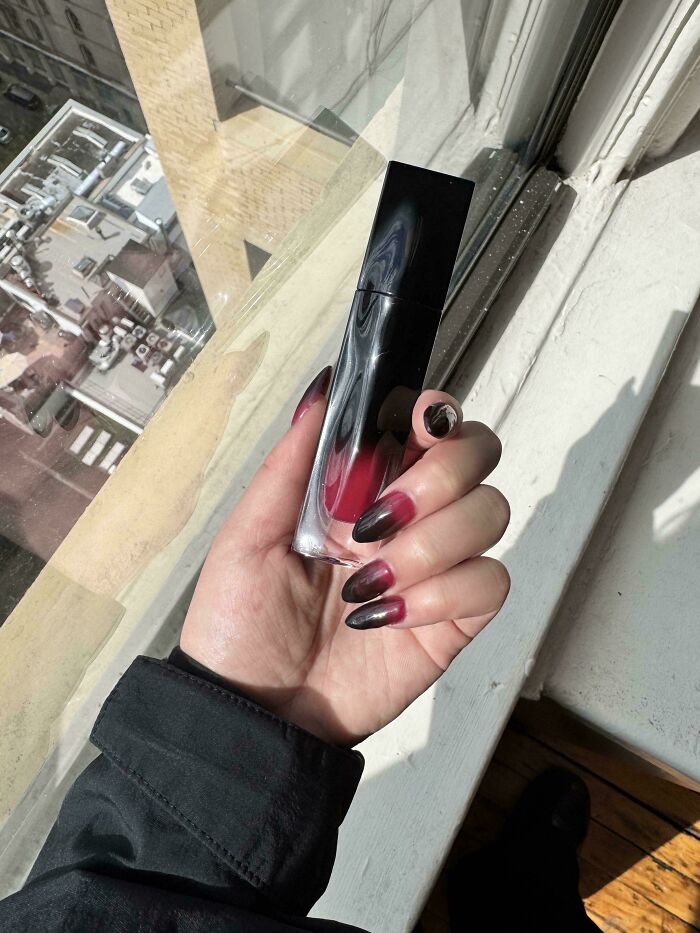 Hand with ombre nails holding a lip gloss, an accidental color match with the product. Satisfying photos lowering cortisol.