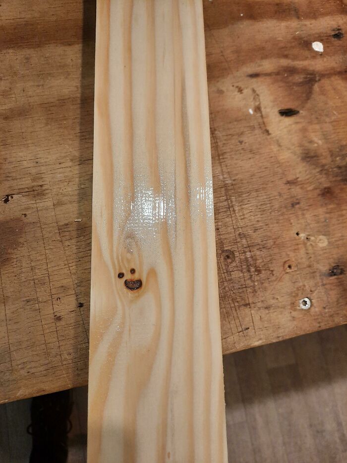 A wholesome pic of a wooden board with a knot resembling a smiling face, next to a darker wooden surface.