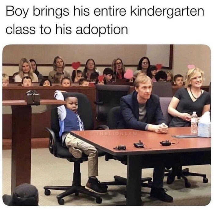 A boy in a suit at his adoption with his kindergarten class behind him, creating wholesome pics.
