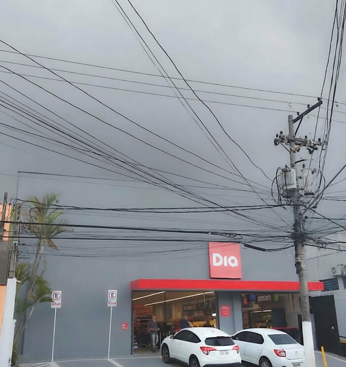 An accidental color match: a grey store facade with a red sign, two white cars, and power lines against a cloudy sky.