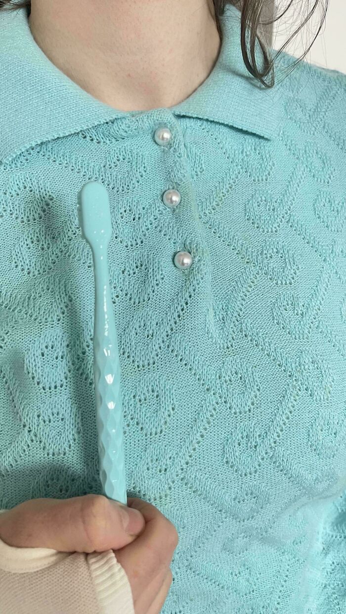 A hand holds a light blue toothbrush that perfectly matches a light blue knitted sweater with pearl buttons. Accidental color matches.
