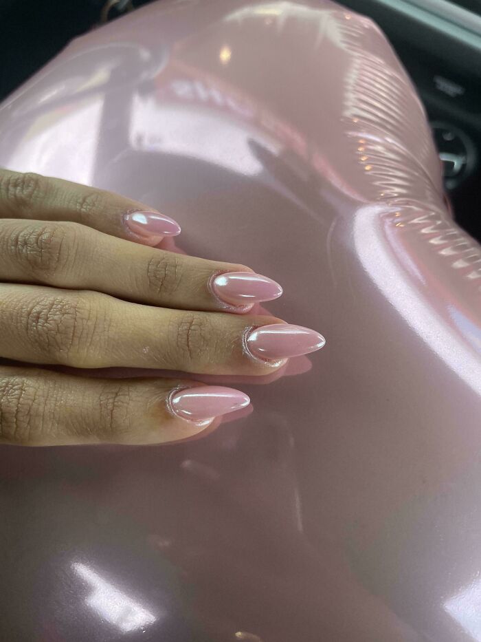 A hand with pink almond-shaped nails matching a shiny pink object, a satisfying photo of an accidental color match.