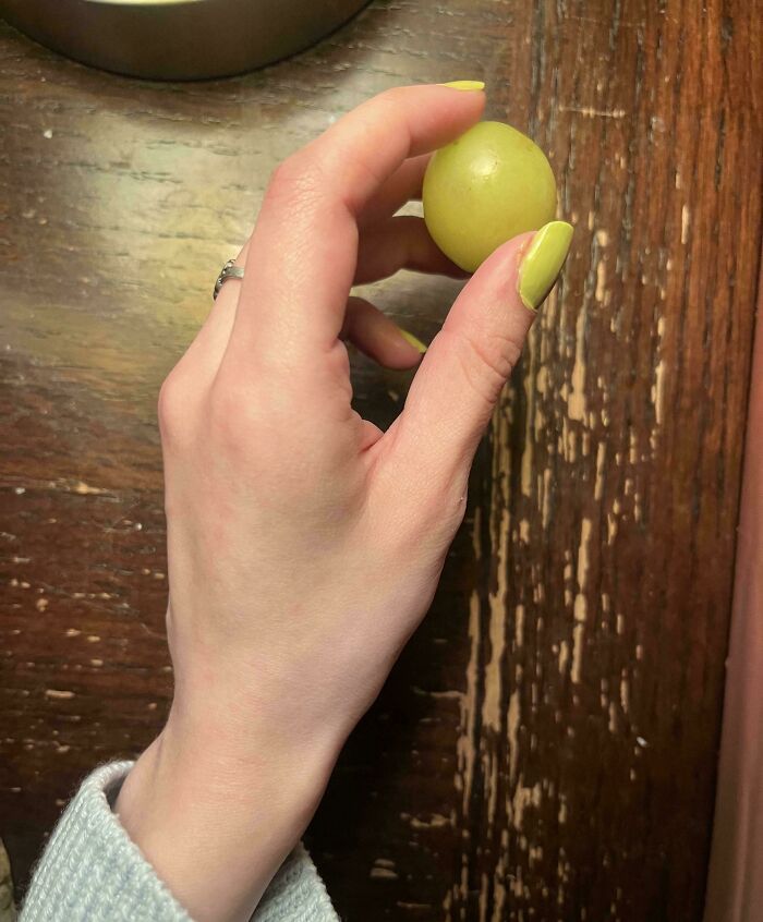 A hand with lime-green nail polish holds a grape, matching the polish for an accidental color match that may lower cortisol levels.
