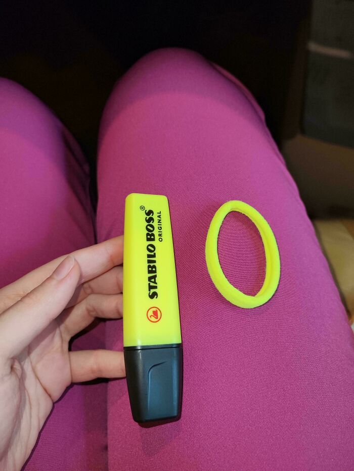 A person holds a yellow Stabilo Boss highlighter next to a matching yellow hair tie on fuchsia fabric, an accidental color match.