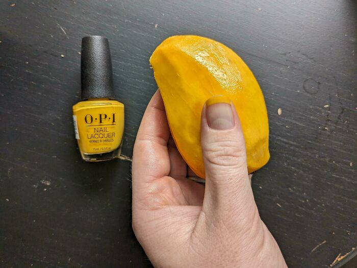 A hand holds a mango peel matching an OPI yellow nail polish bottle, a satisfying accidental color match.