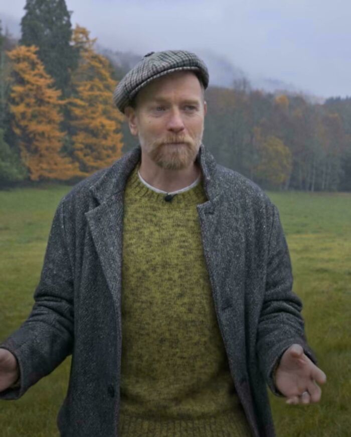 A man with a beard and flat cap, wearing a grey coat and green sweater, in a field with autumn trees, showcasing accidental color matches that may lower cortisol levels.