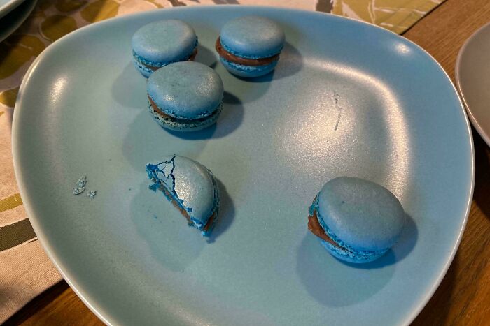 Blue macarons with brown filling on a matching blue plate. One macaron is broken. Satisfying photos for accidental color matches.
