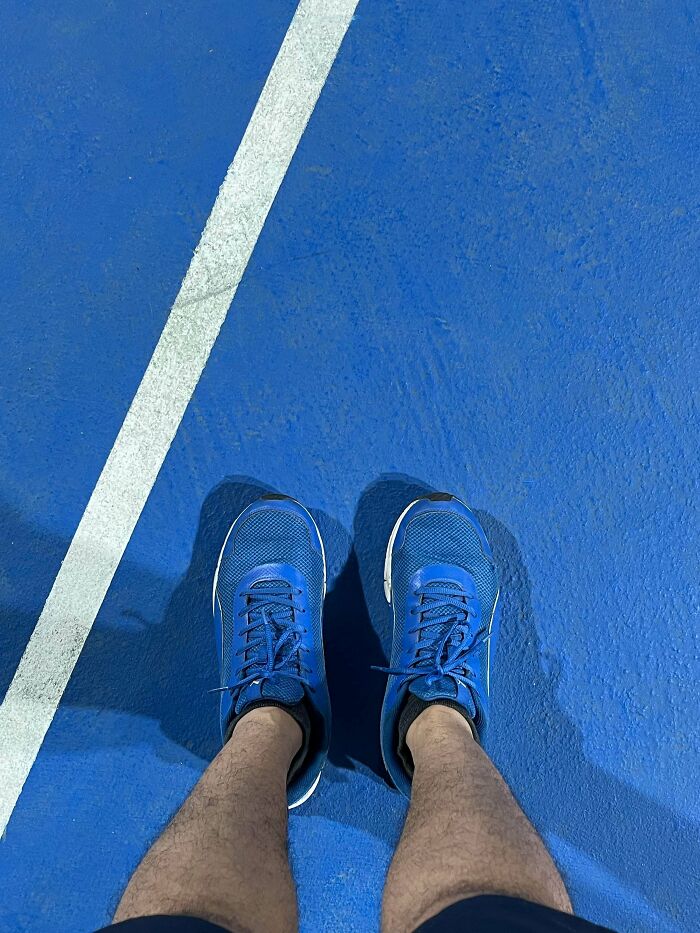 A pair of blue sneakers on a blue court with a white line, a satisfying accidental color match.