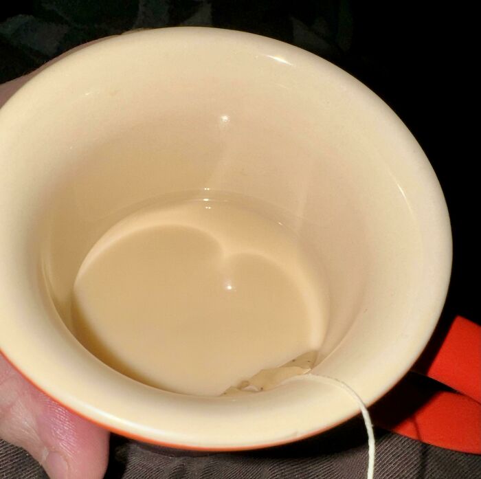 A pale beverage in a cream-colored mug, showing reflections and a teabag string. Satisfying accidental color matches.
