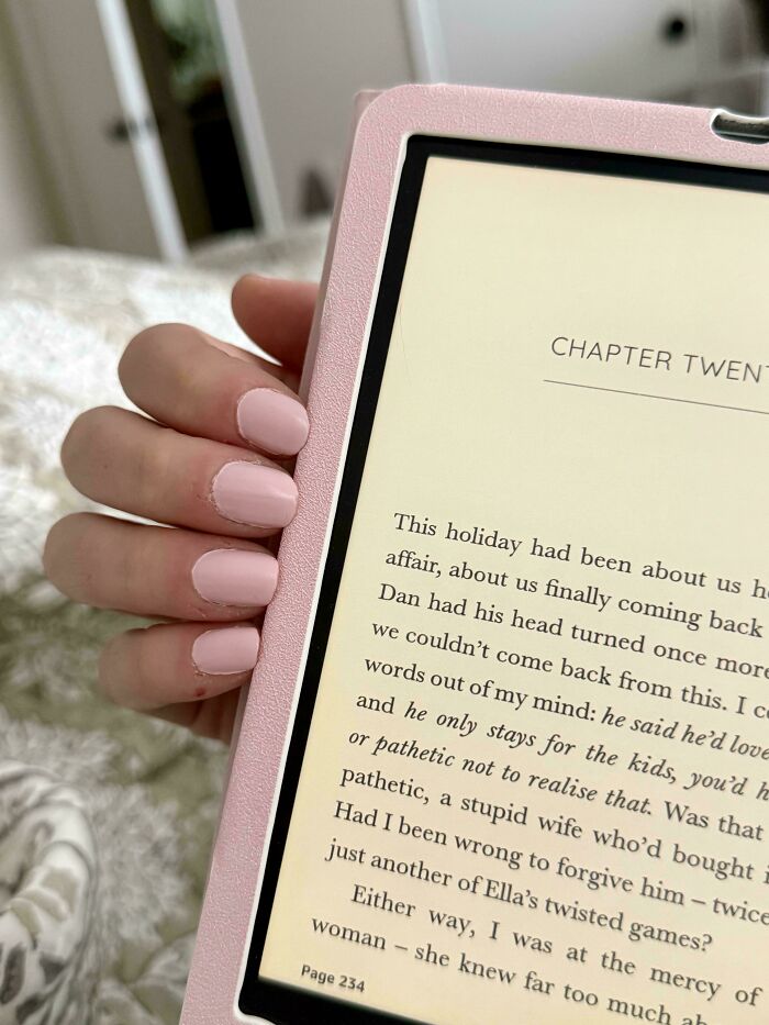 A hand with pink nails holding a pink e-reader, reading a novel. An accidental color match that may lower your cortisol levels.