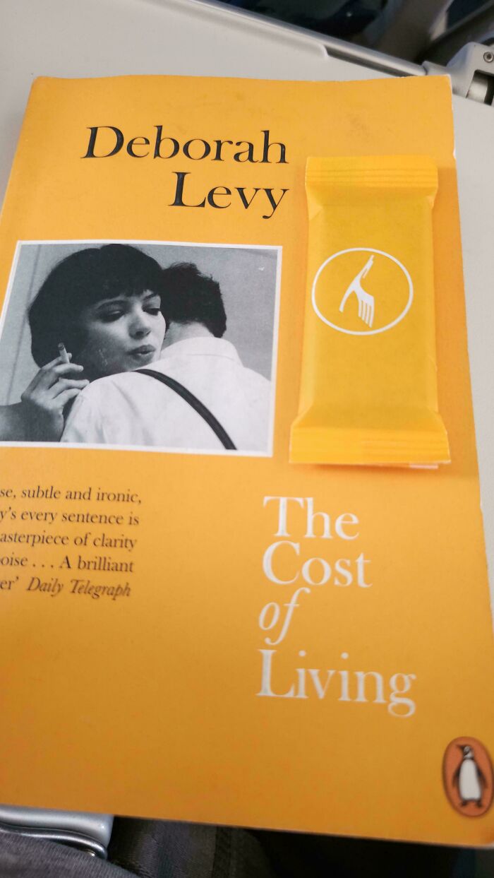 A yellow book, The Cost of Living by Deborah Levy, with a yellow mini-candy bar on top. Accidental color matches that may lower your cortisol levels.