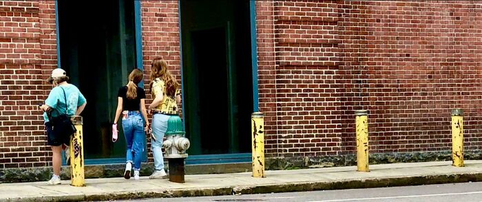 Three people walk past a brick building with yellow poles and a green fire hydrant; an accidental color match.