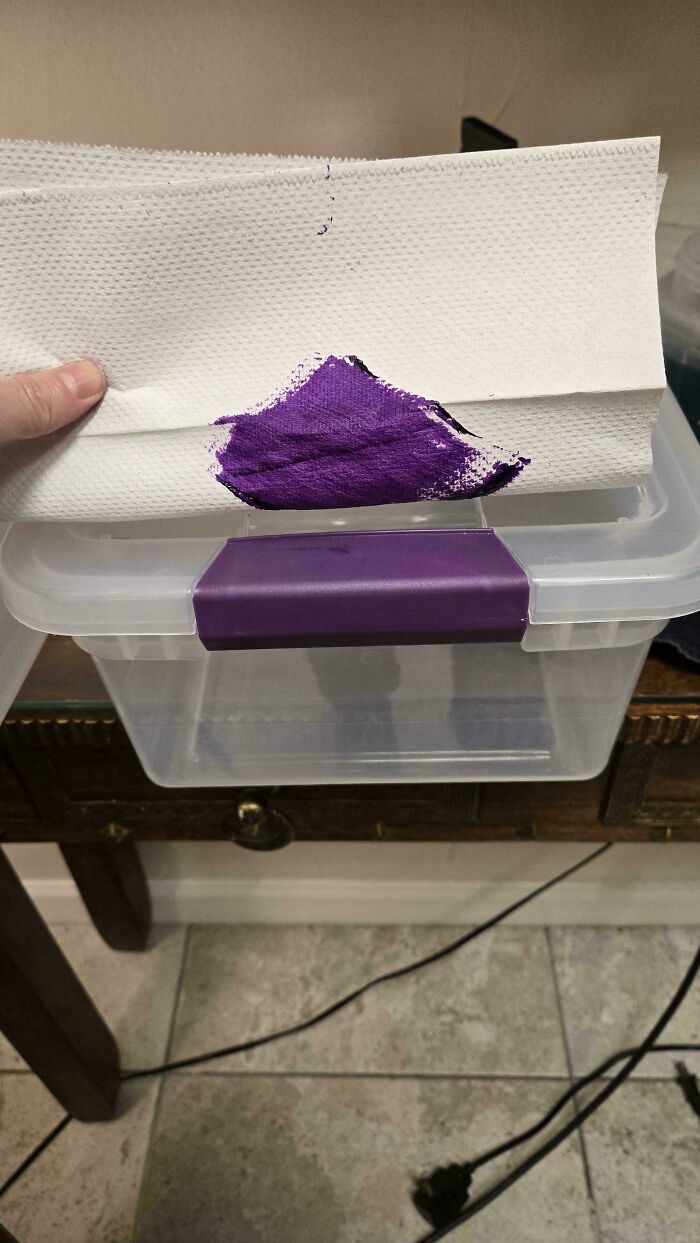 A satisfying accidental color match: vibrant purple paint on a white paper towel aligning perfectly with a purple latch on a clear plastic container.