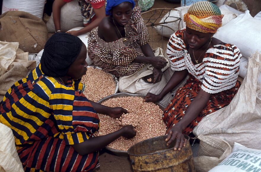 Three women sorting dried peanuts in metal bowls and burlap sacks. This image relates to countries with the worst diets.
