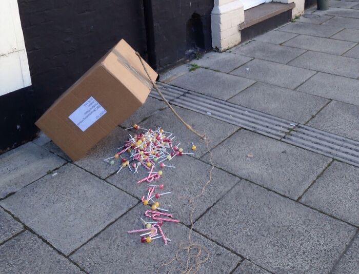 A cardboard box overturned on a sidewalk, spilling numerous colorful lollipops. A scene of doctors' awesome sense of humor.