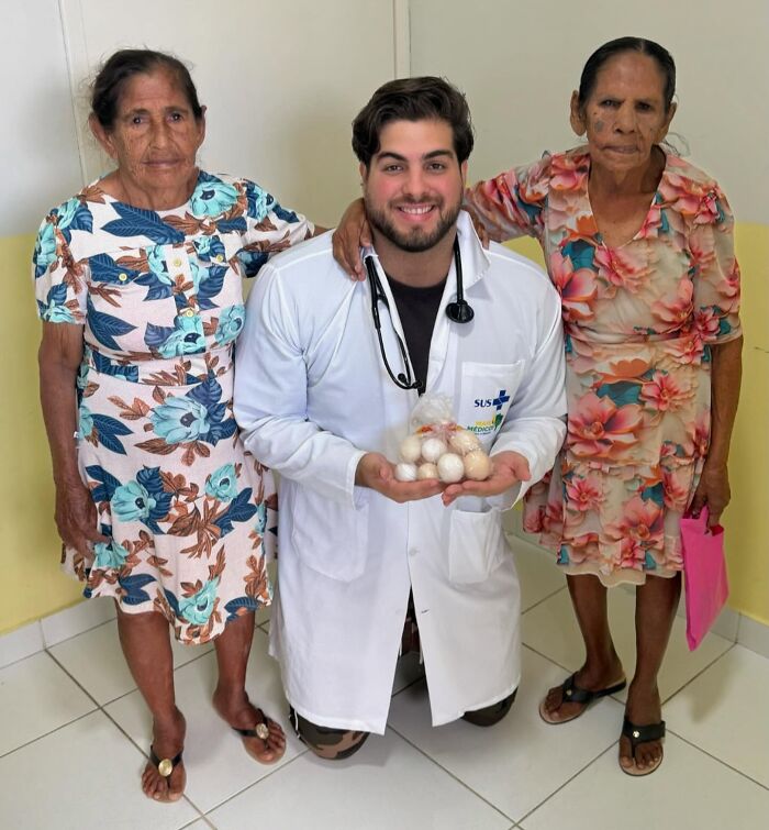 A doctor with awesome sense of humor kneels, holding eggs, flanked by two elderly women, making healthcare less scary.