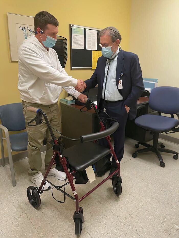 A doctor in a suit and mask shakes hands with a younger man holding a walker. Doctors' awesome sense of humor.