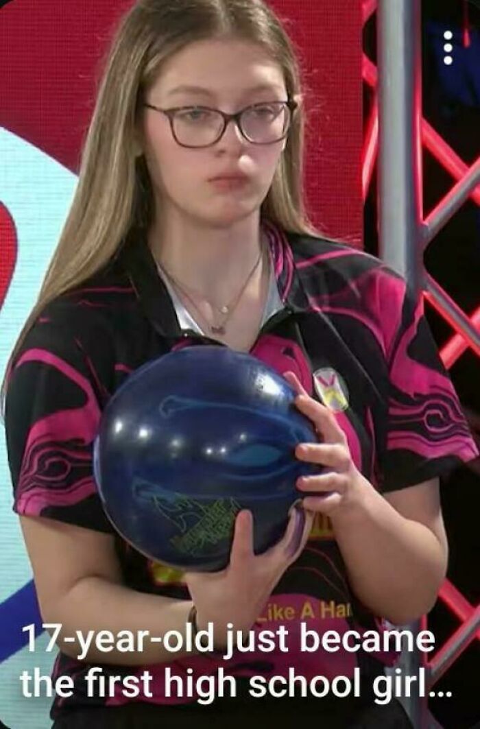A young bowler with glasses, wearing a pink and black shirt, holding a blue bowling ball. This image could suffer from premature truncation.