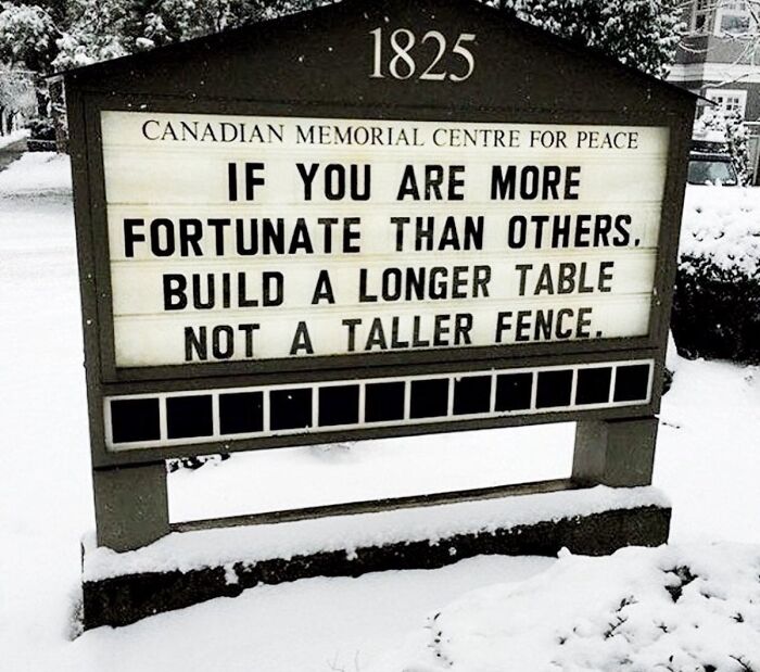 A wholesome pic of a Canadian Memorial Centre sign in snow, displaying the message: Build a longer table, not a taller fence.