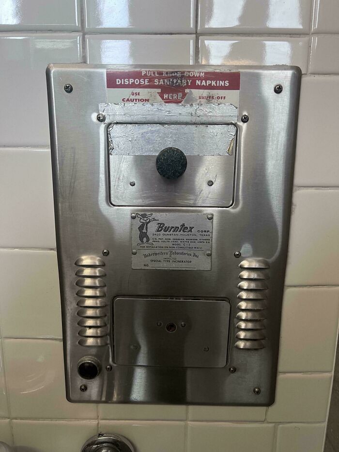 Vintage sanitary napkin incinerator mounted on bathroom tiled wall