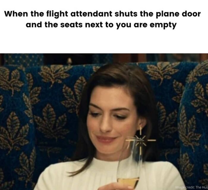A woman subtly smiles, holding a drink on a plane, portraying the joy of empty adjacent seats. Travel memes for your desk.
