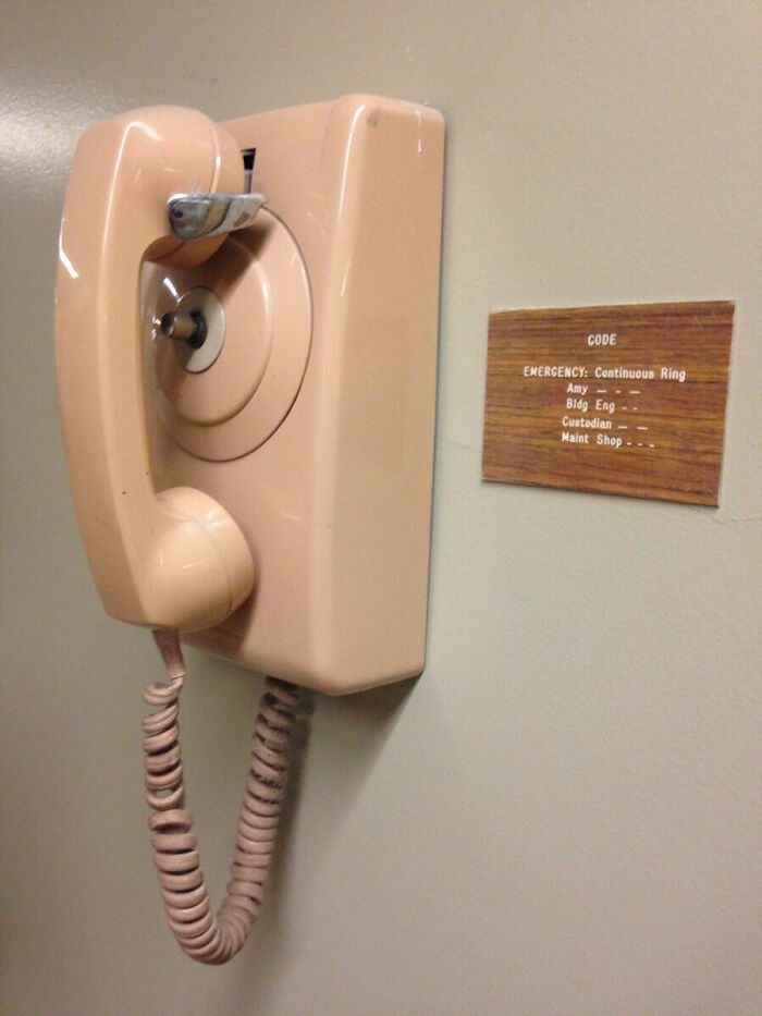 Vintage beige telephone with emergency code instructions mounted on school wall