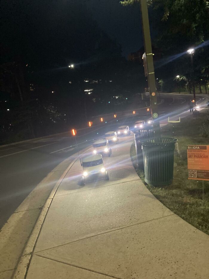 Line of small golf carts with headlights on at night on campus pathway