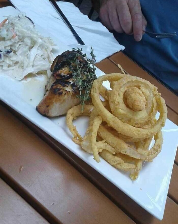 Dinner plate with grilled chicken and onion rings forming a face pareidolia