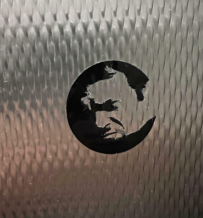 Pareidolia face formed by worn sticker on textured metal surface