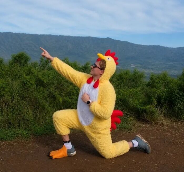 A person in a chicken suit, kneeling and pointing, with a mountain landscape behind them, a funny proposal pic edit.