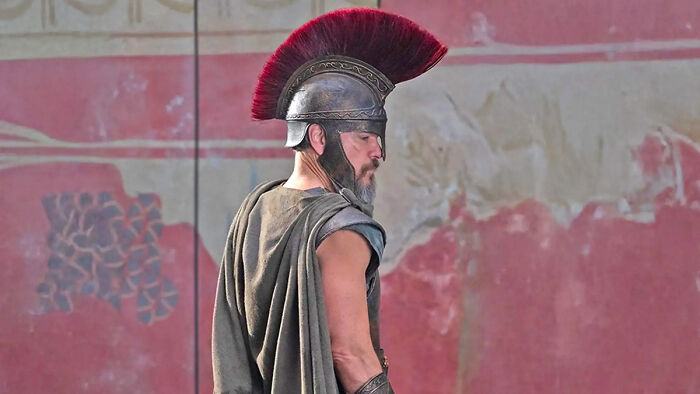 Um homem com barba e capacete e capa de soldado romano. O debate sobre o filme Odisseia.