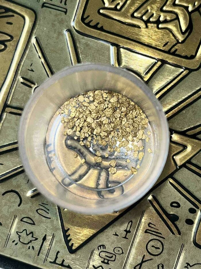 Pile of gold flakes in a small clear container on engraved golden surface